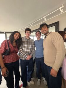 Four friends posing for a photo indoors, smiling at the camera in casual clothing.